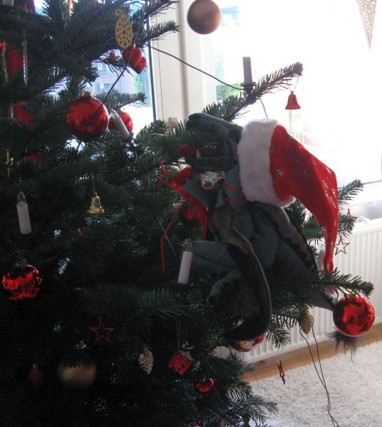 Drache mit Weihnachtsmütze klettert im Tannenbaum herum