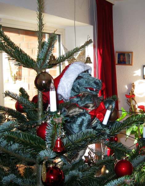 Drache mit Weihnachtsmütze sitzt gemütlich im Tannenbaum